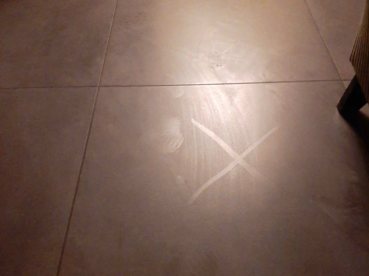 A floor surface with a visible sign X indicating that there is dirt on the surface even though the floor surface is cleaned.